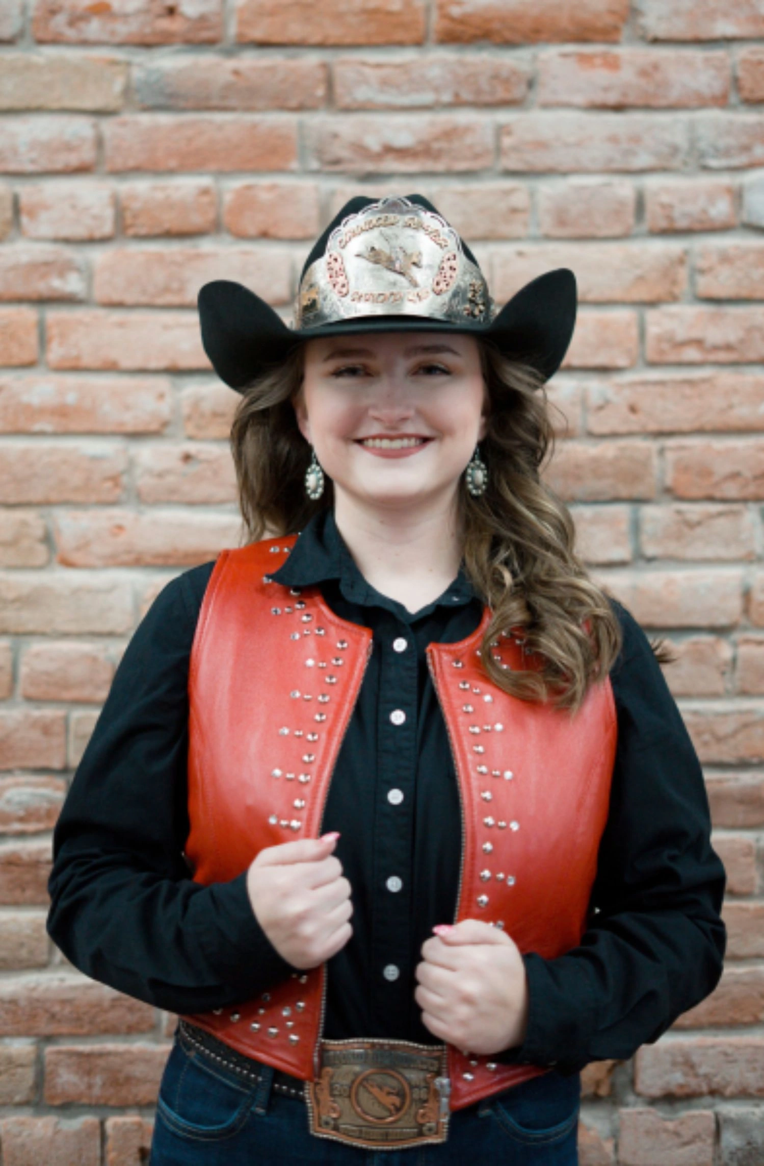 Photo of 2026 Queen Aubrey in black hat with medallion, black oxford, and red leather vest